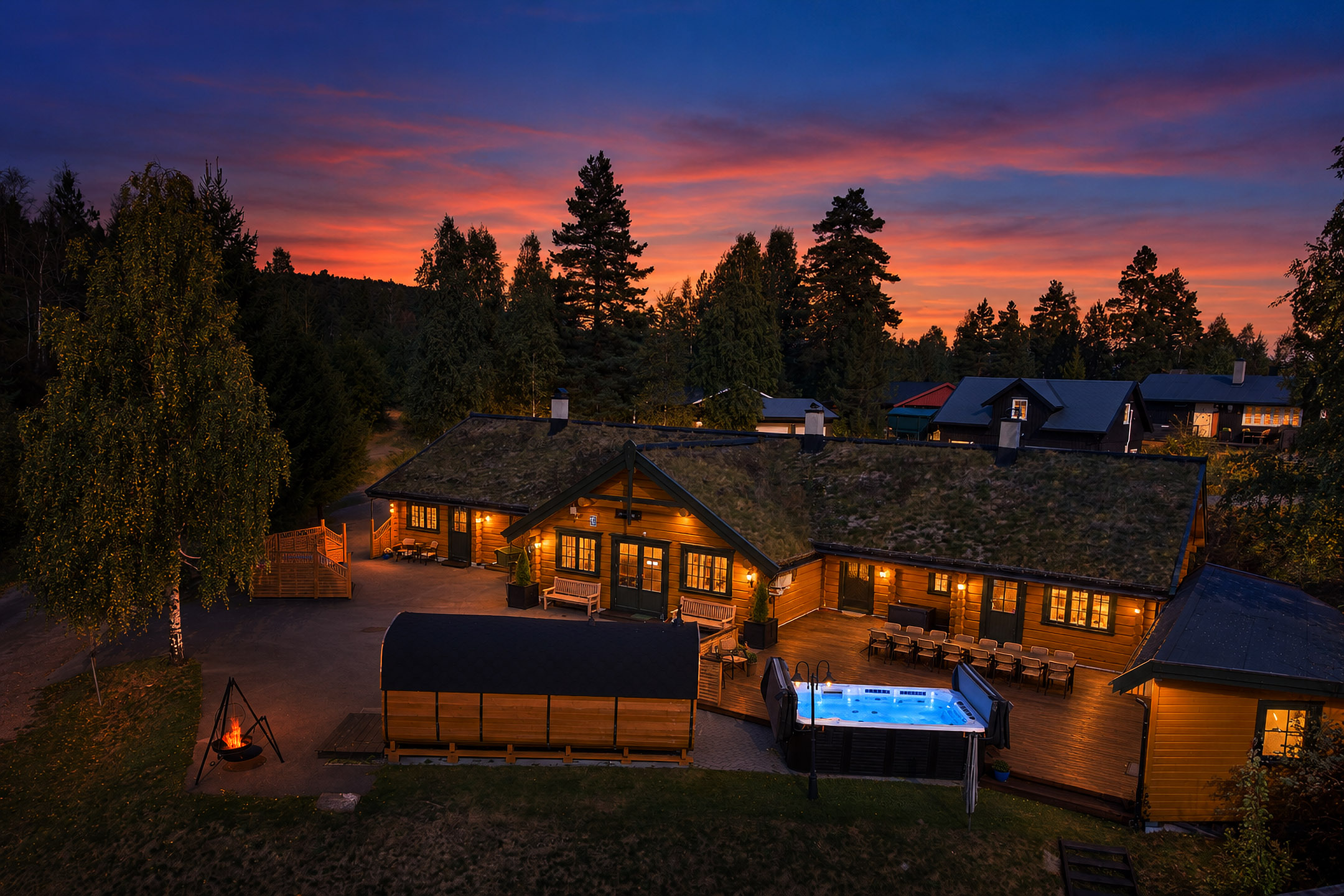 Lågen Lodge i Svarstad ved solnedgang, med opplyste tømmerhytter, badstue, jacuzzi og bålpanne.